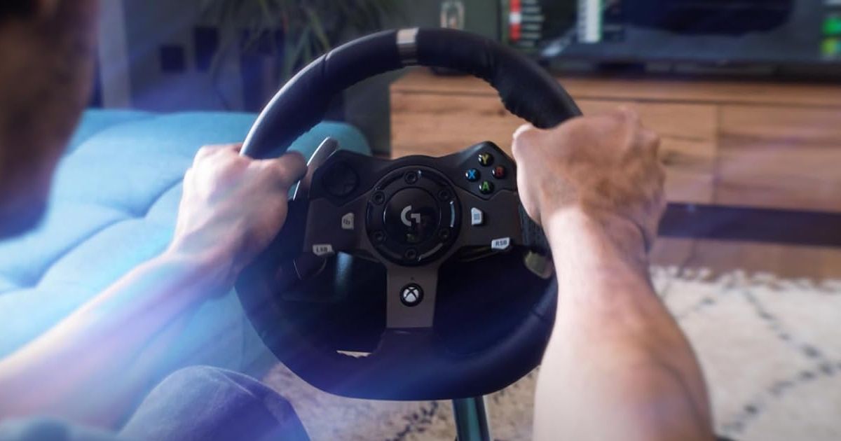 Someone using a black Logitech racing wheel in front of a TV.