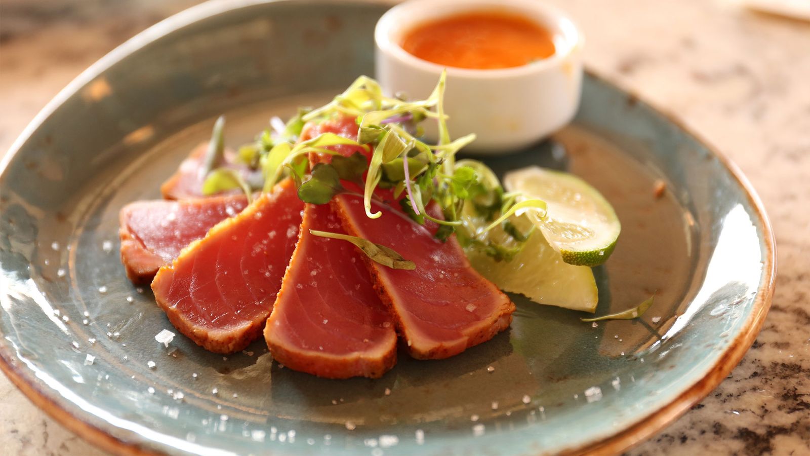 Seared tuna on a light blue plate with salad and sauce.