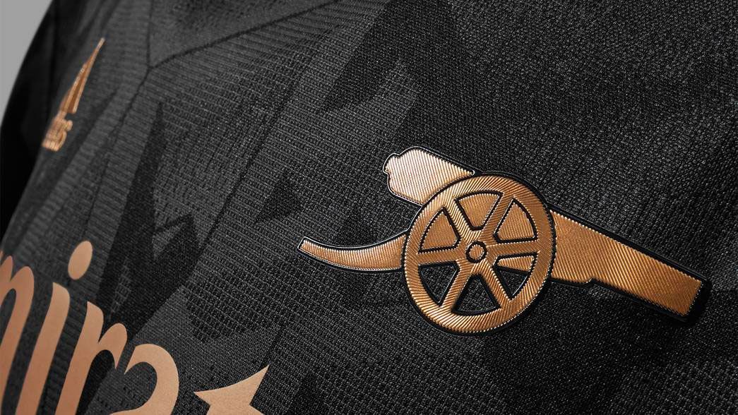 Arsenal away kit 2022/23 product image of a black shirt with metallic copper/gold details.