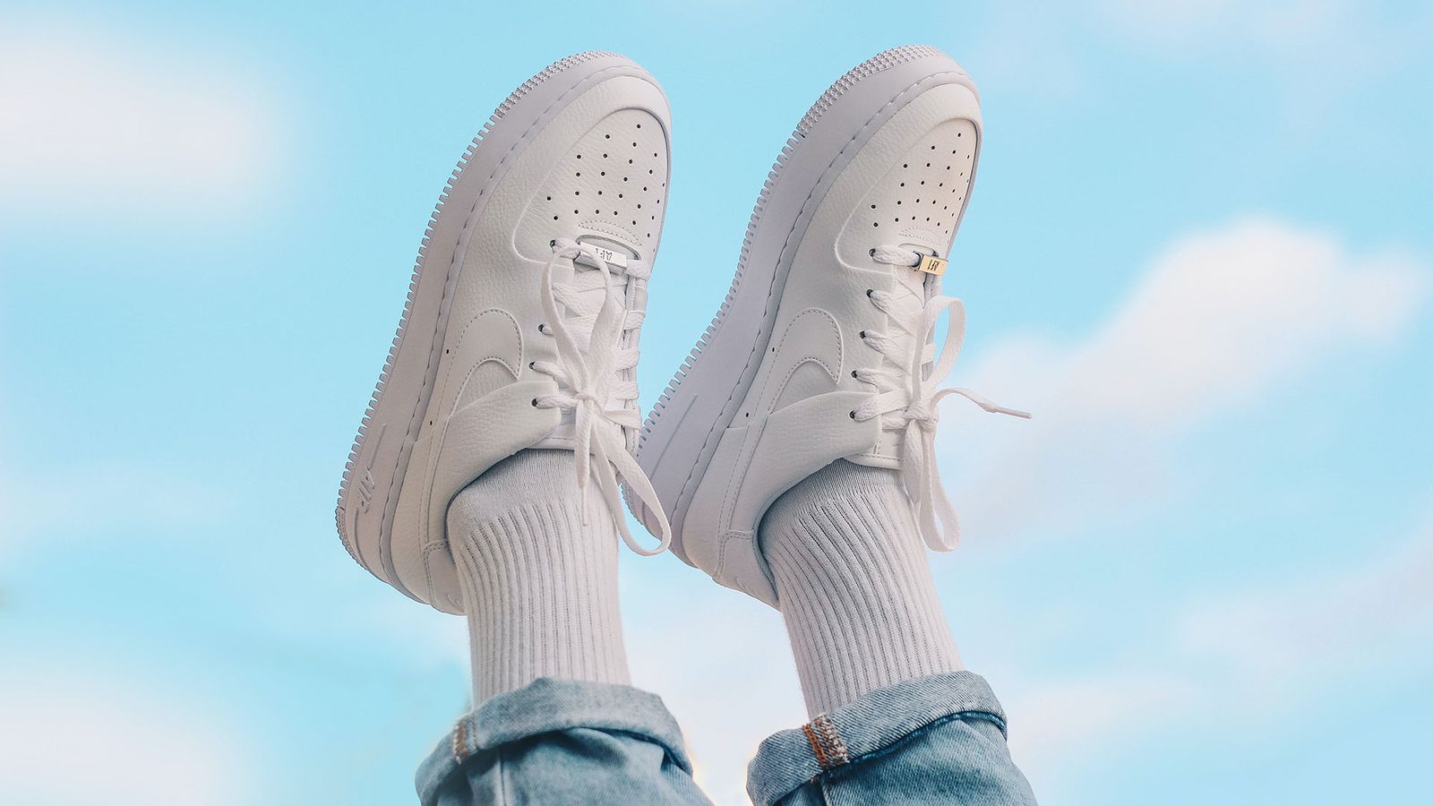 Person in blue jeans wearing white Air Force 1 Lows and sticking them in the air.