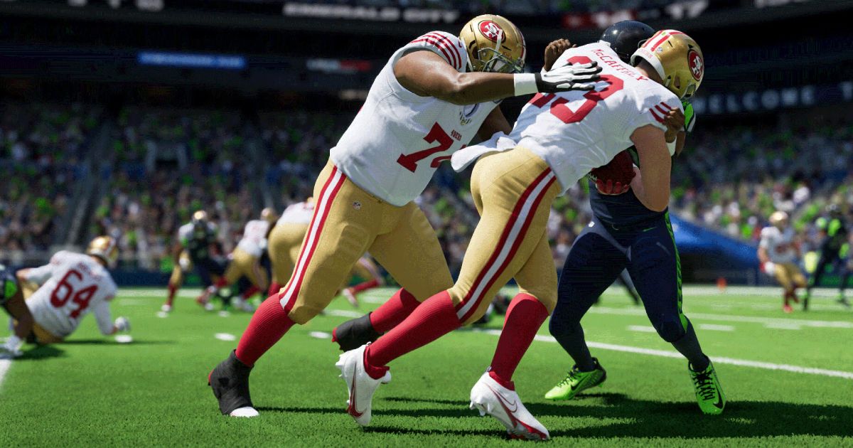 Two NFL players in white jerseys and gold leggings with red trim driving against an opponent.