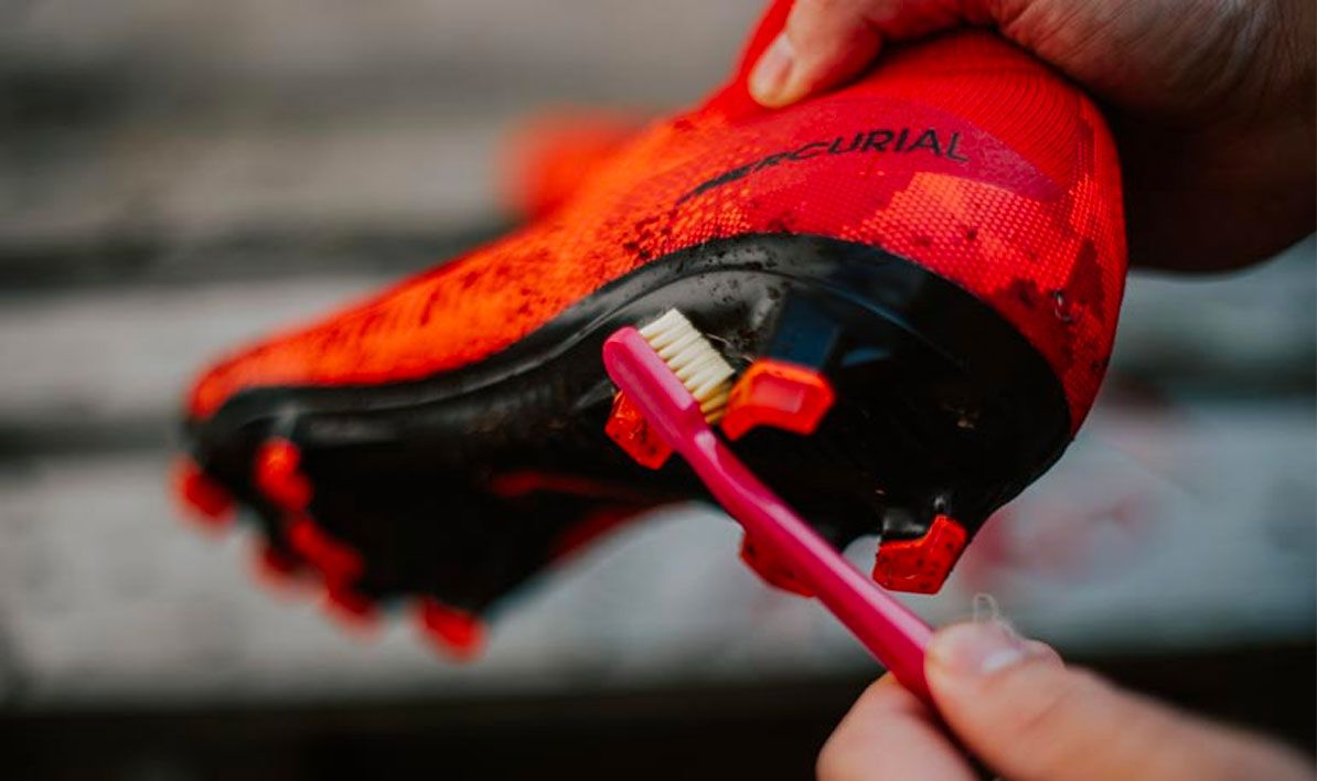 How to clean football boots image of orange Nike Mercurial boots being cleaned with a toothbrush.