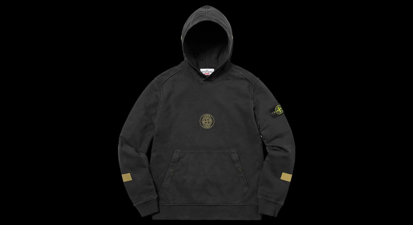 Supreme x Stone Island Hooded Sweatshirt product image of a black jumper with a golden Supreme x Stone Island logo in the centre.