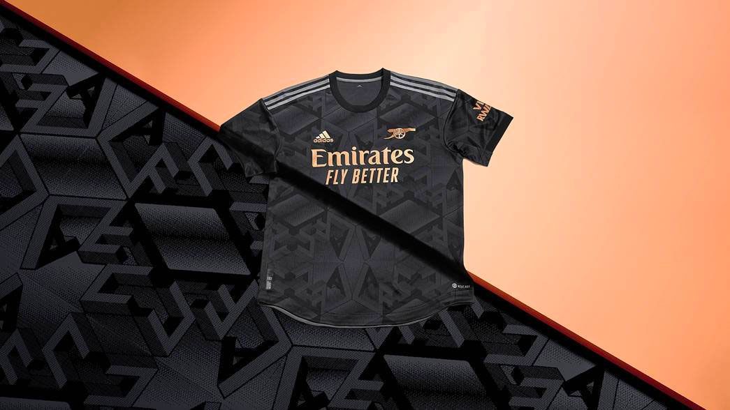 Arsenal away kit 2022/23 product image of a black shirt with metallic copper/gold details.