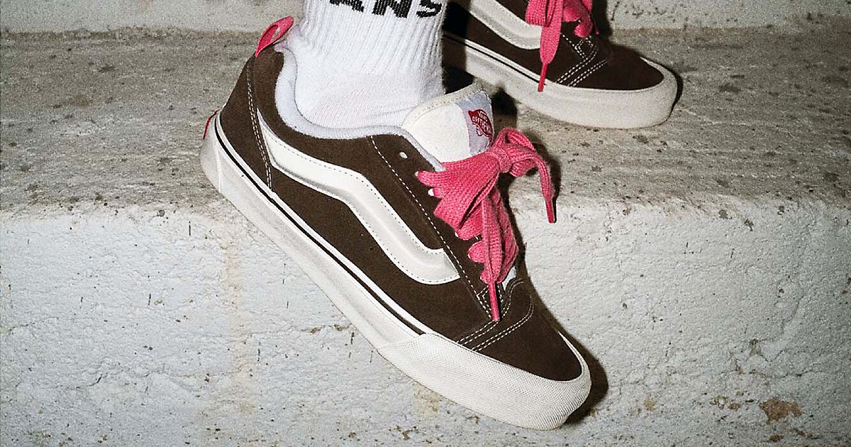 Someone in white Vans socks wearing a pair of brown suede Knu Skool low-tops with white details and bright pink, chunky laces.