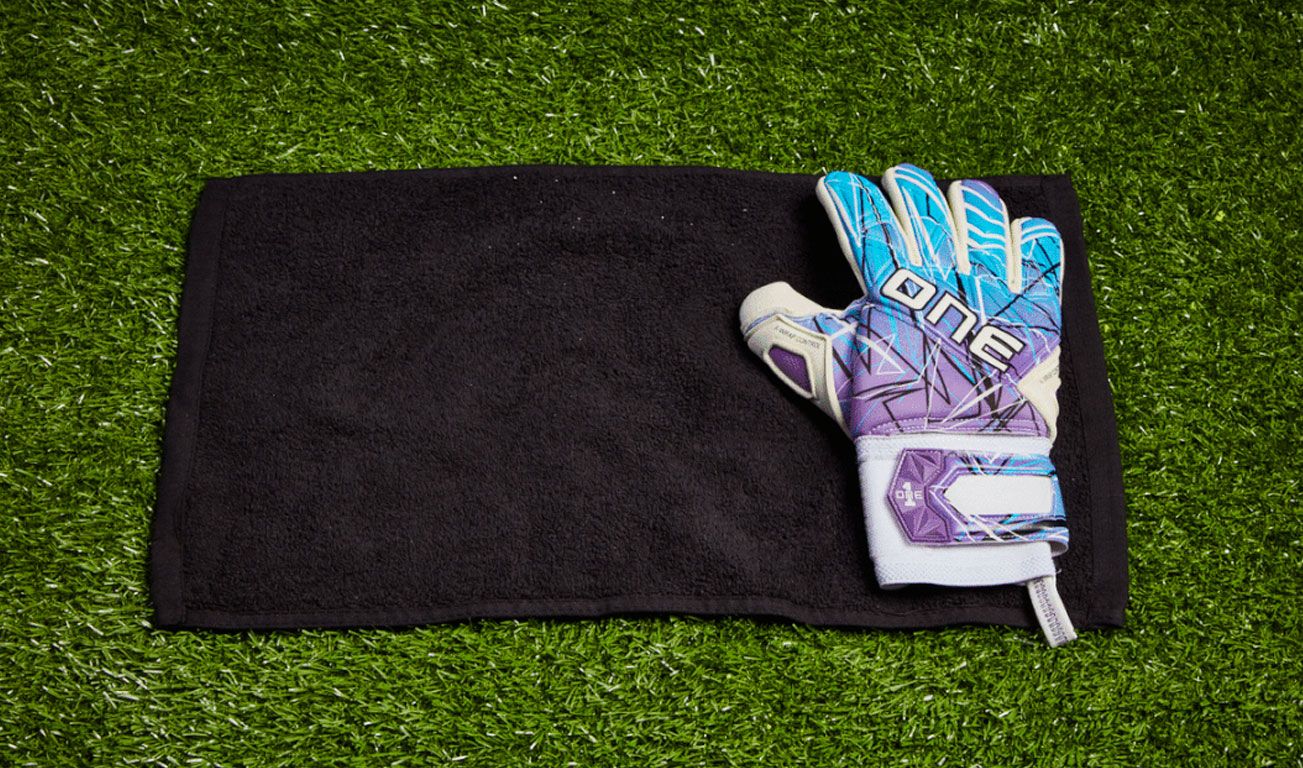 Drying a white One goalkeeper glove with purple and blue details in a black towel.