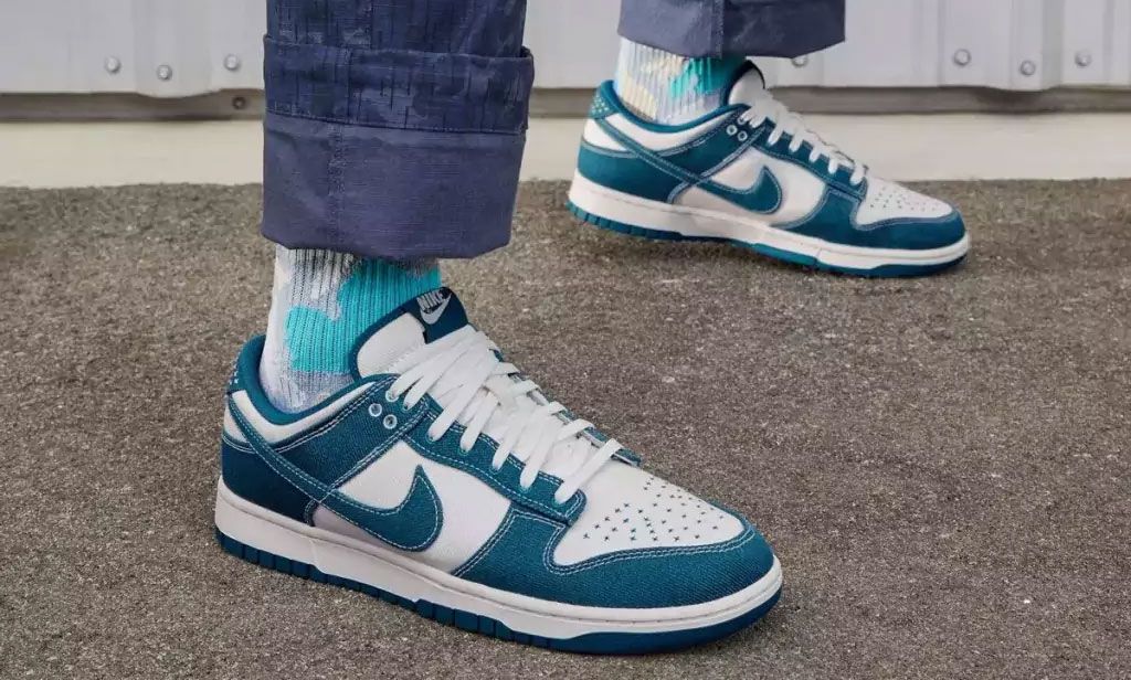 Someone in blue trousers and white and blue tie-dye socks wearing blue canvas and white leather Nike Dunk Lows.