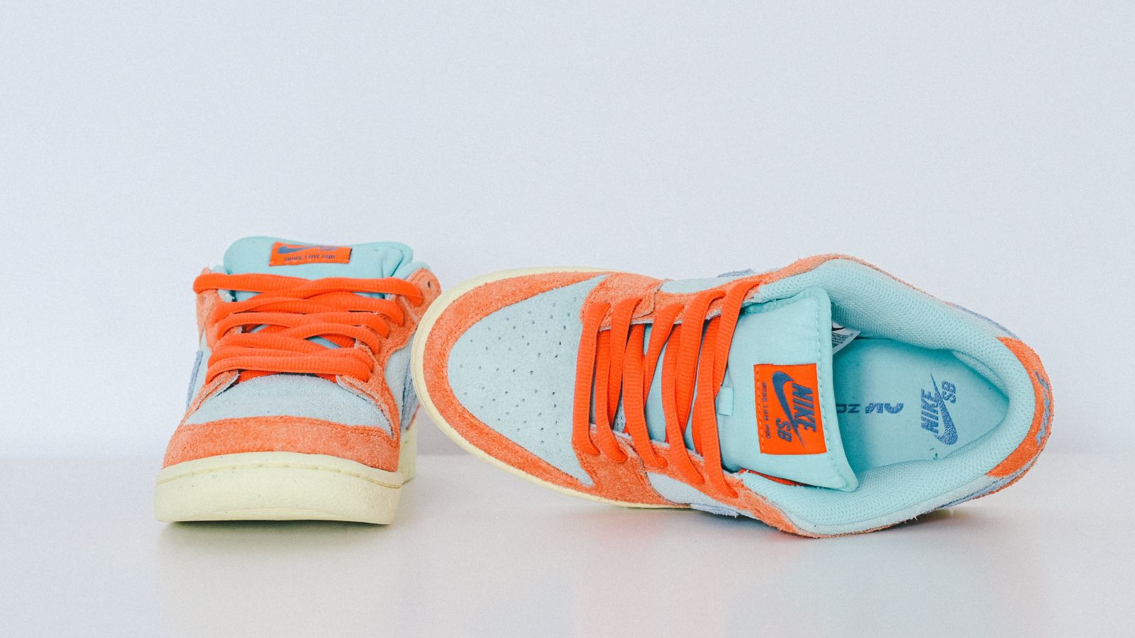 A pair of orange and light blue Nike SB Dunks featuring cream midsoles and loosely tied orange laces.