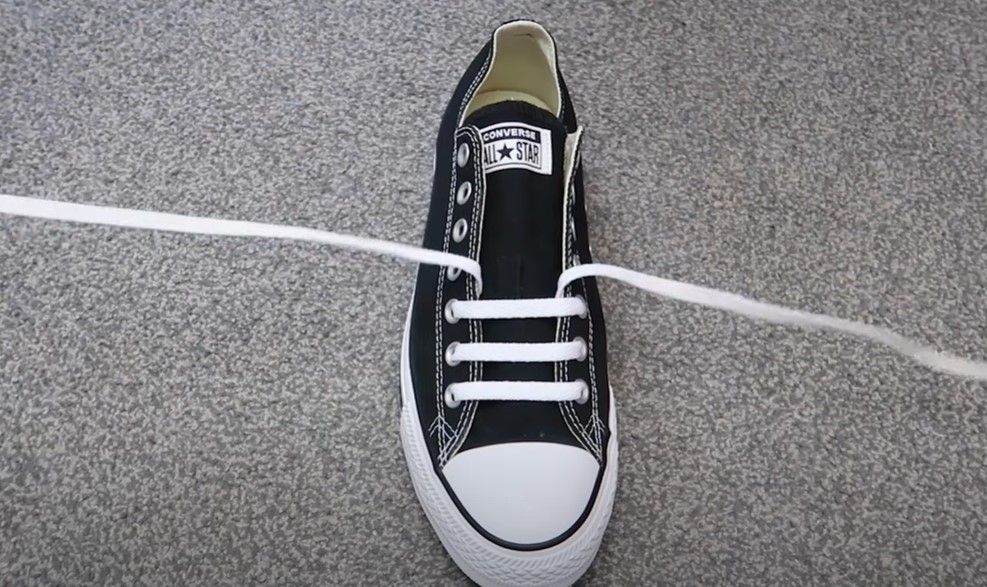 Image of a black Converse sneaker with white laces straight over the tongue.