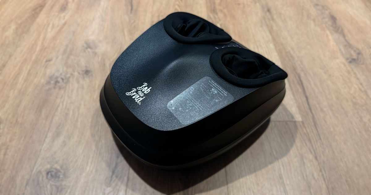 A black foot massage machine on a light wood floor.