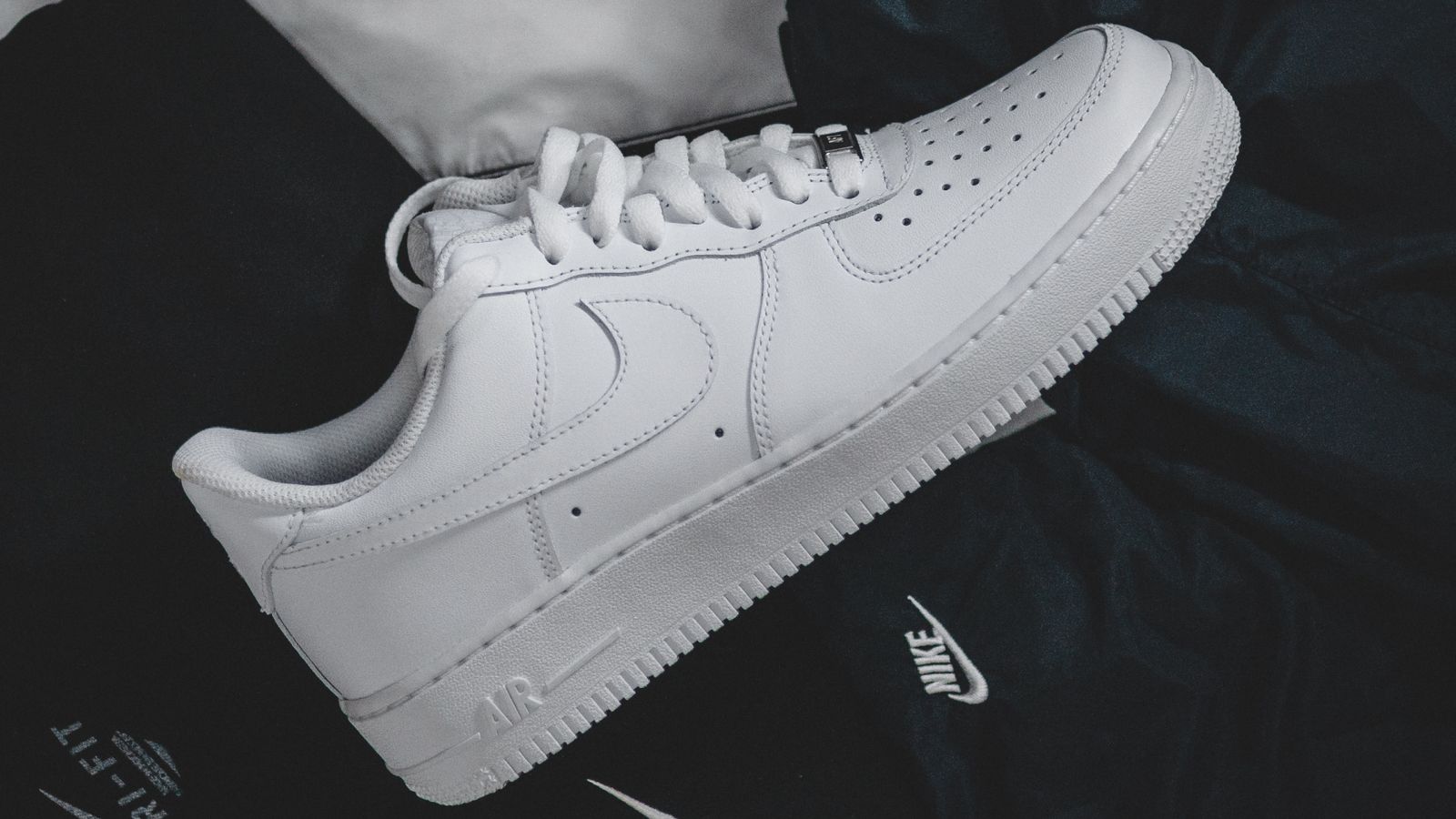 A white Air Force 1 on bed of black Nike clothing.