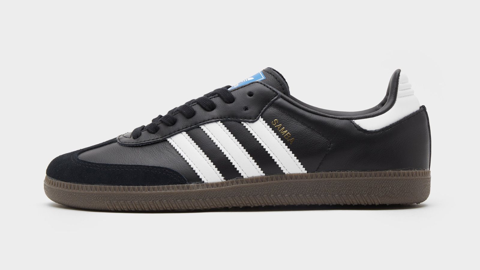 adidas Samba OG "Black White" product image of a black low-top shoe featuring white stripes down the side, gold Gazelle branding, a blue logo on the tongue, and a gum sole.