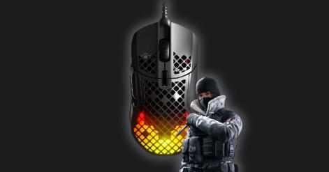 A black SteelSeries gaming mouse with yellow and red lighting inside that shines through the honeycomb exterior. The mouse has Frost, a character from Siege, next to it.