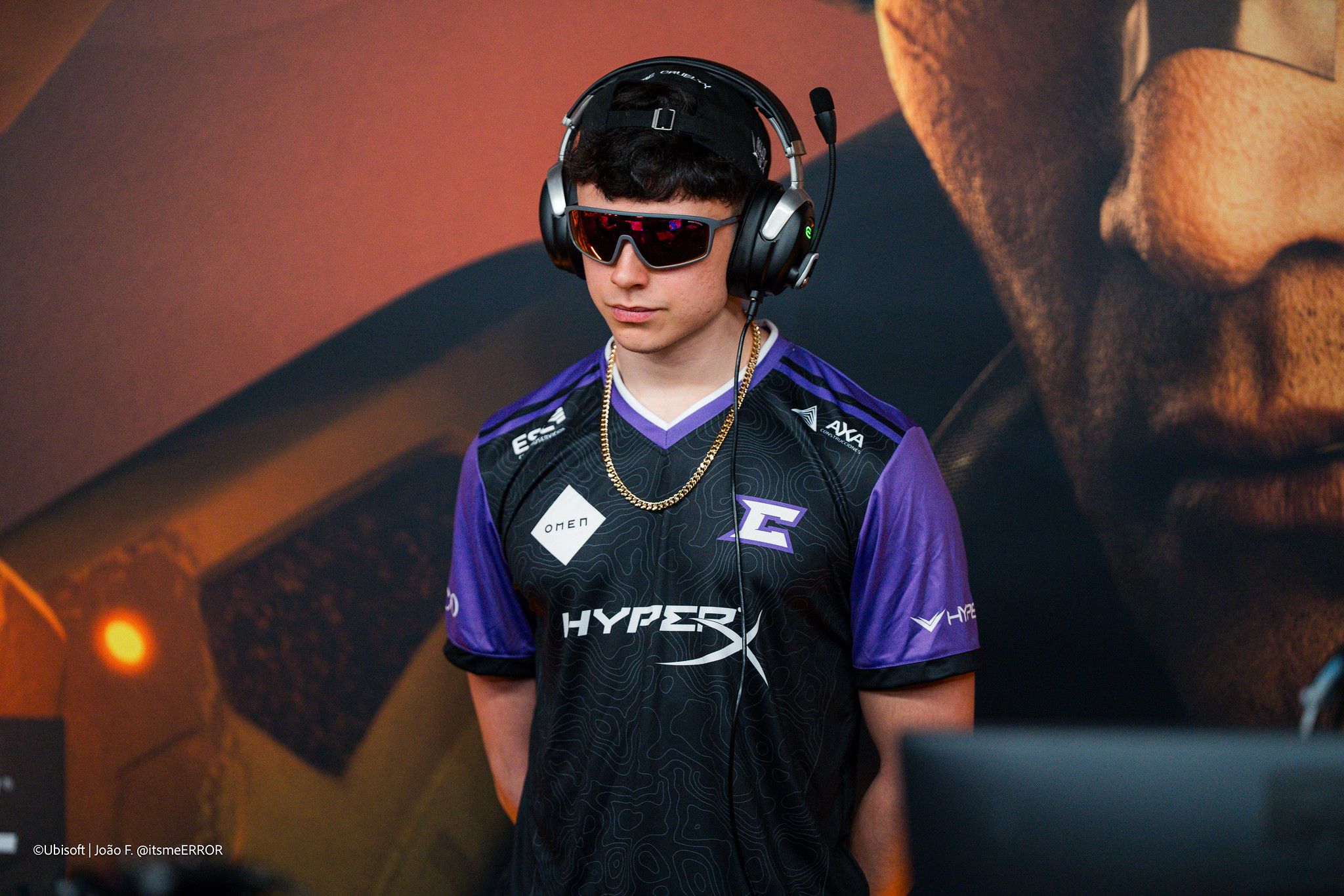 a young man wearing headphones and sunglasses is standing in front of a computer monitor .