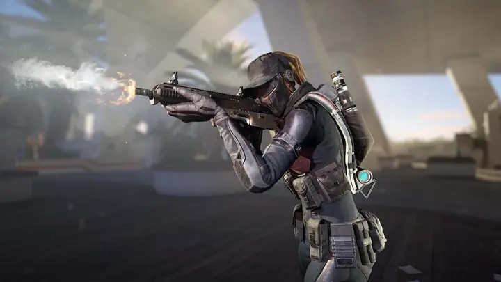 XDefiant key art shows a feminine Phantom character wearing a dark outfit and cap aiming and firing an assault rifle to the left.