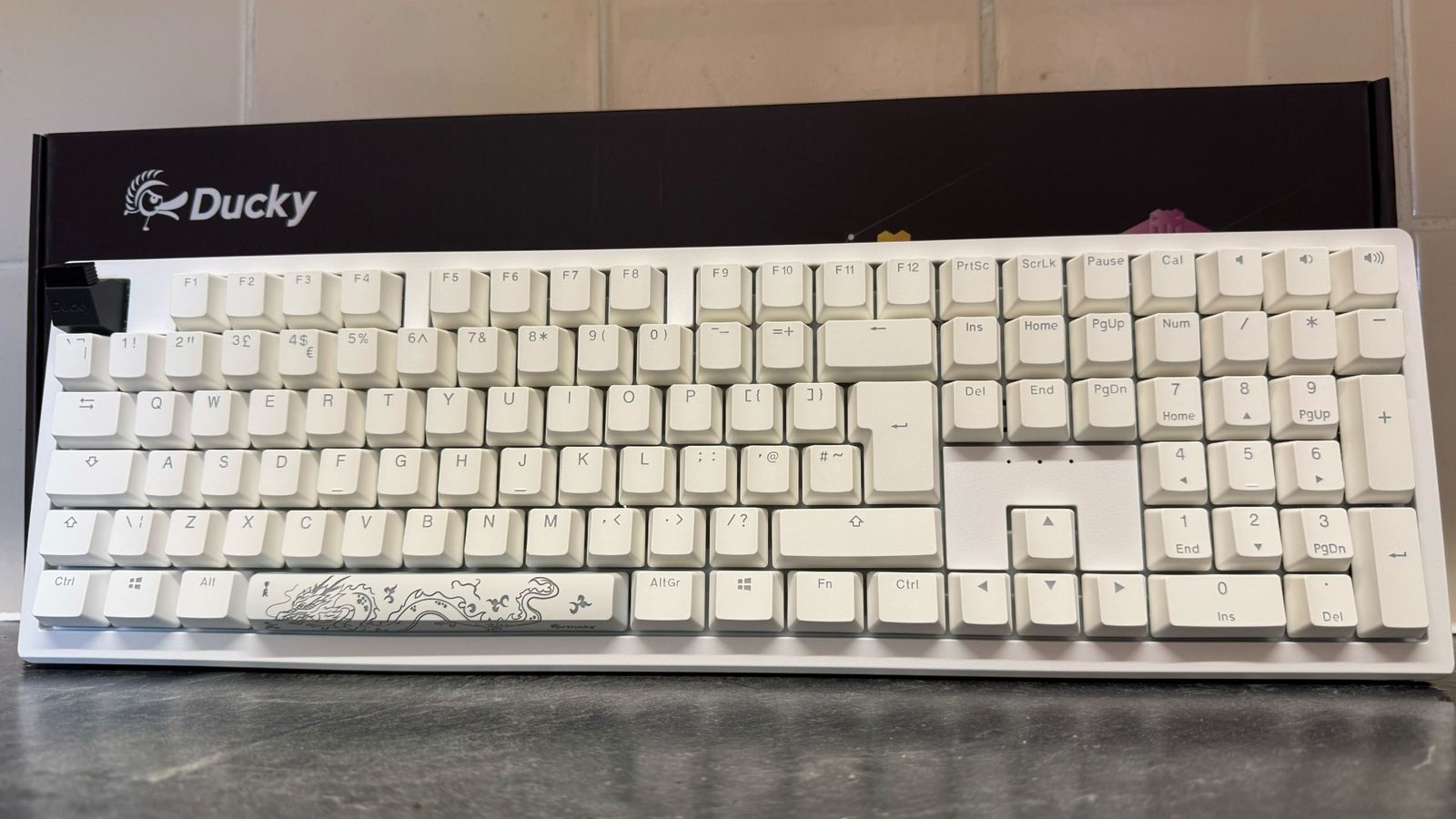 Ducky Zero 6108 in an all-white colorway in front of its box and a tiled wall