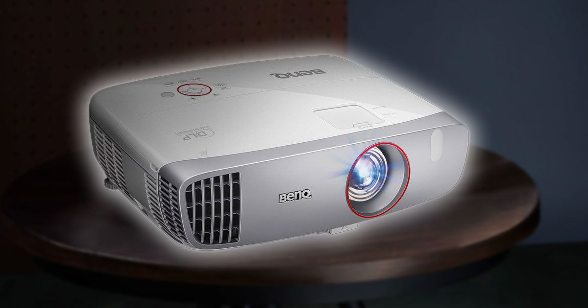 A white BenQ projector sitting on top of a dark brown wooden table with a white glow around it.