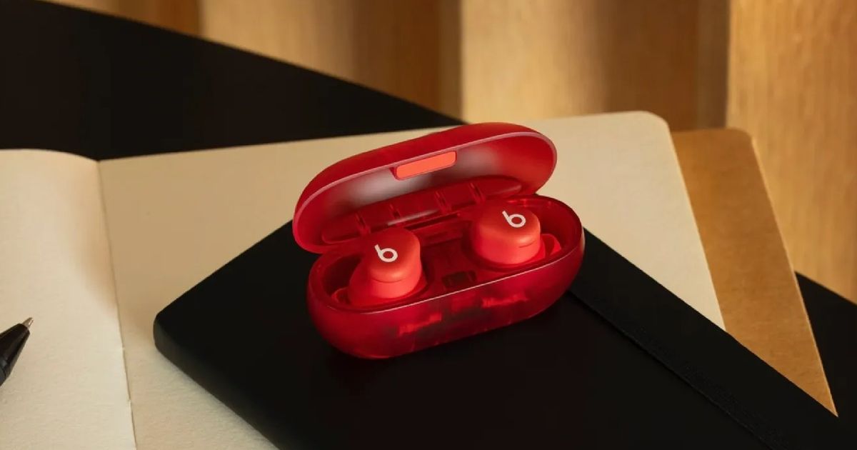 A pair of red Beats Solo Buds (2024) in their charging case, sitting on a desk and a notebook