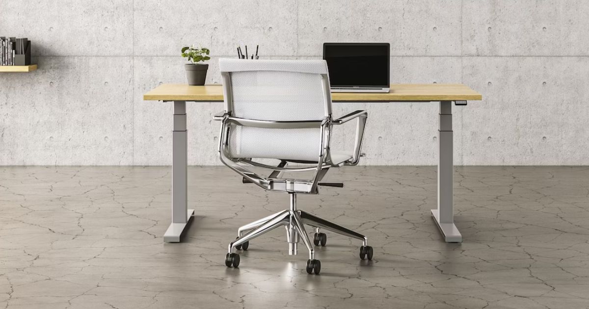 A grey office chair sat in front of a light brown and grey desk with a laptop on top.